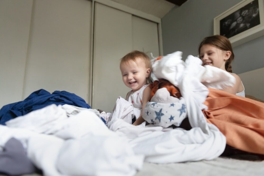 Happy emotional kids rush and play in a pile of clothes on the bed, chaos at home with children