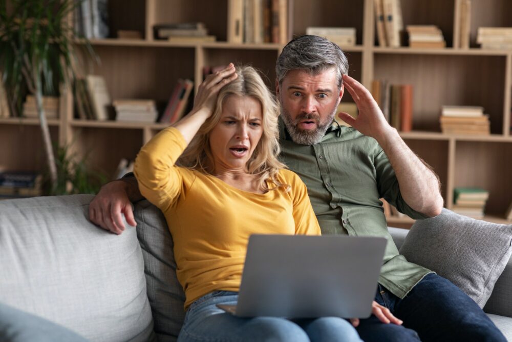 Online Scam. Emotional middle aged couple looking at laptop screen with shock